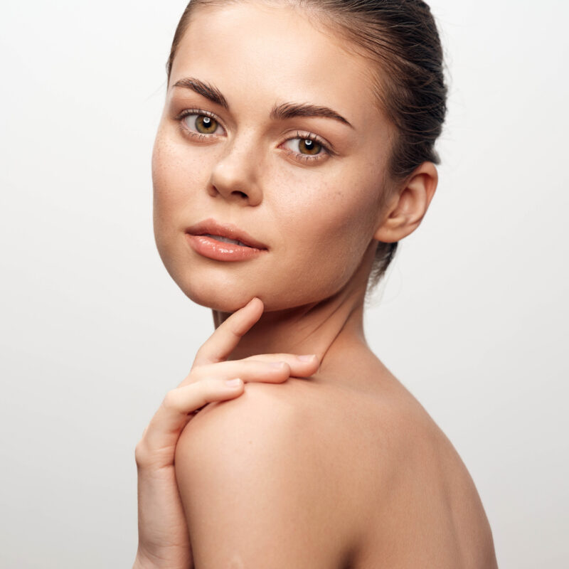 Attractive young woman with charming pose looking directly at camera with hands on chin in beauty and fashion concept portrait