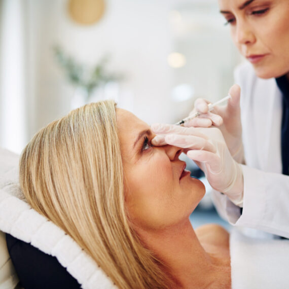 Young female doctor performing a botox injection to the forehead of a mature woman lying on a table in a beauty clinic