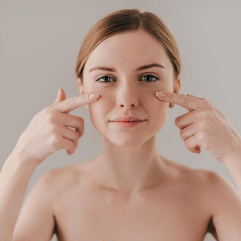 Perfect face. Beautiful young woman looking at camera and touching her face while standing against background