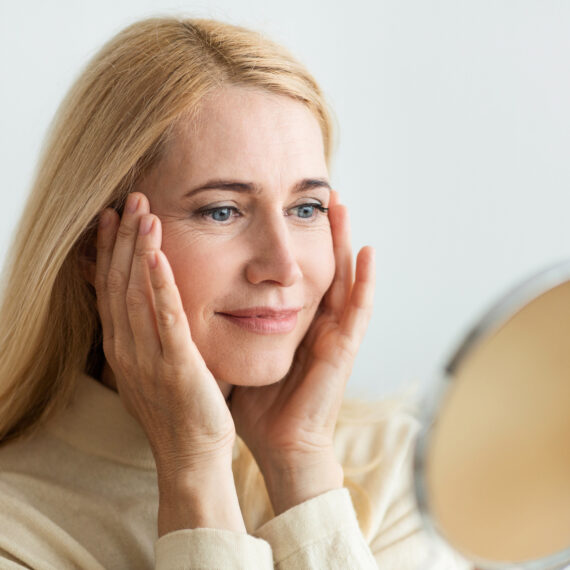 Perfect skin. Middle-aged woman satisfied with her skin, looking at round mirror